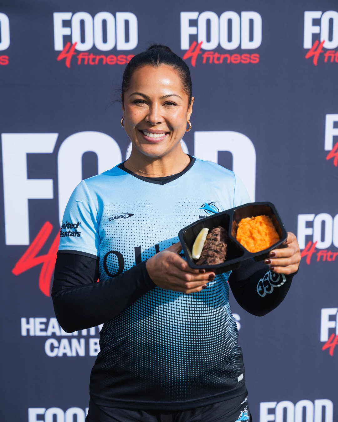 Cronulla Sharks NRLW player holding a Food4Fitness meal in front of a Food4Fitness backdrop
